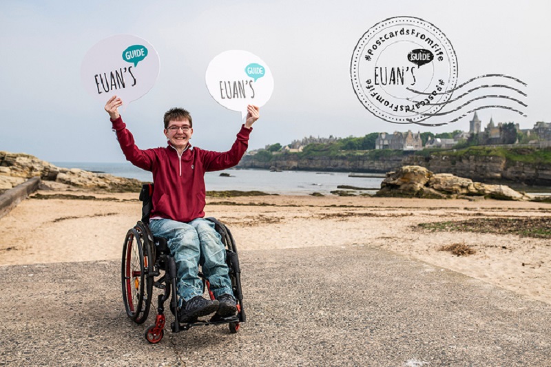 A postcard from Fife showing Chelsea, a wheelchair user, at the beach in St Andrews holding Euan's Guide logos.