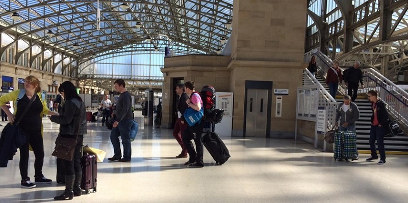 Photo of crowd walking in train station with suitcases.