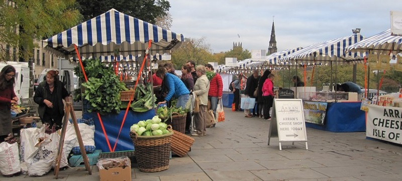 Photo of Edinburgh's market outdoor cheese and vegetable stalls and people shopping.