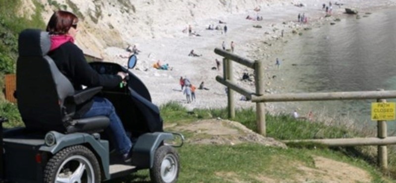 Photo of a woman using an off-road mobility scooter at Lulworth Cove, England.