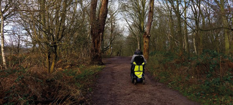 A power chair user pictured travelling along a forest path