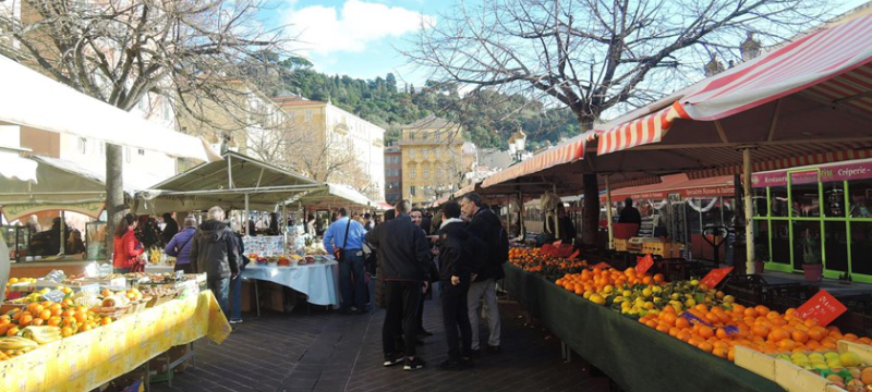 Image of a market in Nice, there are stalls on either side selling various vegetables and fruits.