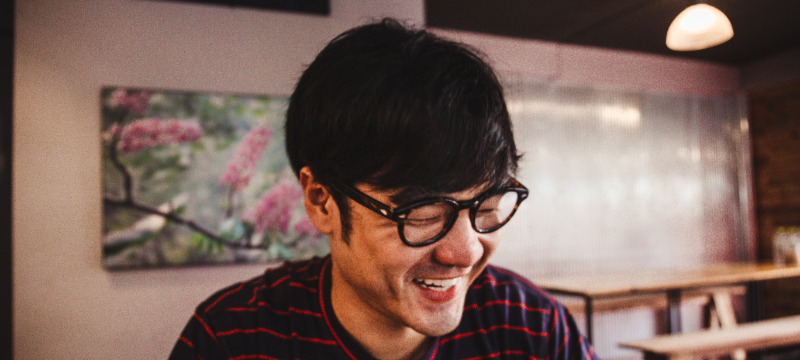 A man wearing glasses is laughing and looking down.