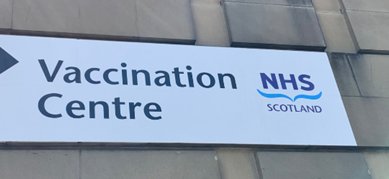 Image of an NHS sign on the side of a wall that says Vaccination Centre