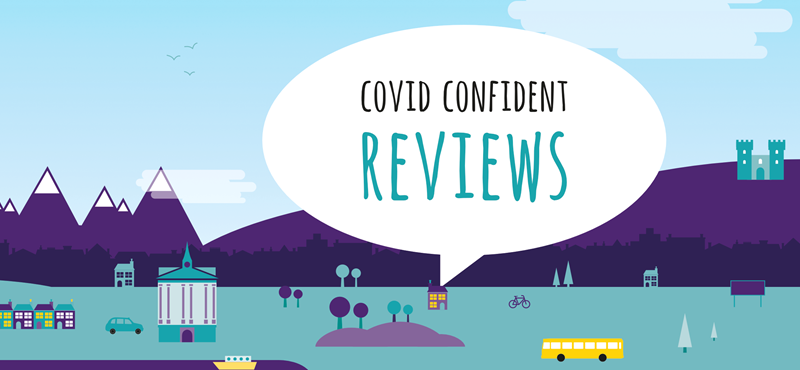 A city graphic illustration of buildings, cars, public transport, mountains, castles, a hot air balloon and houses. Text in the speech bubble says "Covid Confident Reviews"