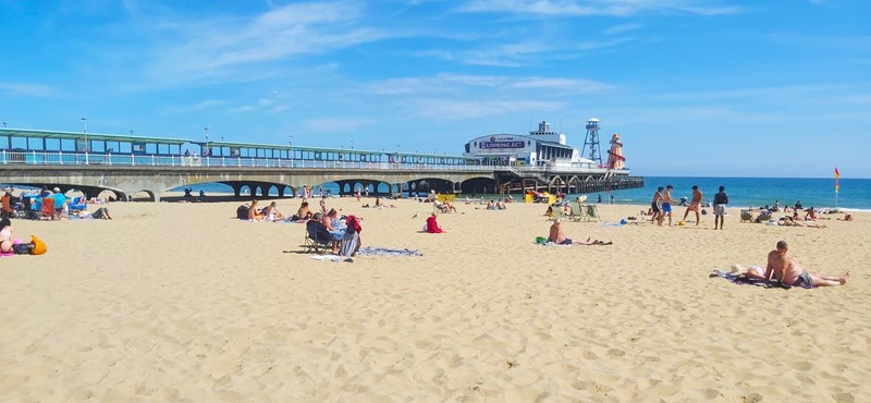 A sandy beach at Bournemouth with a pier and people sunbathing