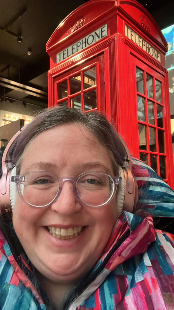 Vikki wears headphones and sits in front of a red telephone box.