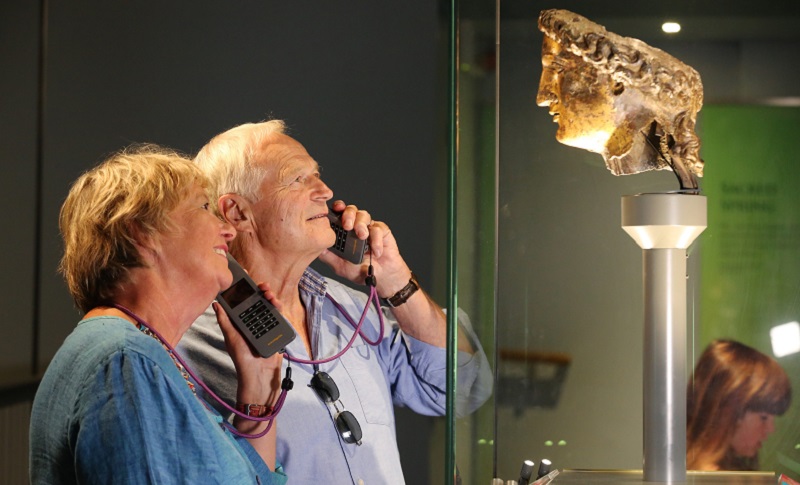 Photo of a couple using audio guides at the Roman Baths.