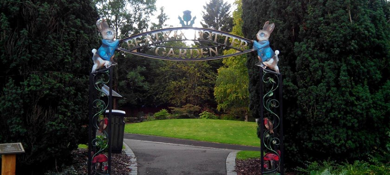 Photograph of garden with level path and a "Beatrix Potter Garden" sign with two Peter Rabbit drawings on each side.
