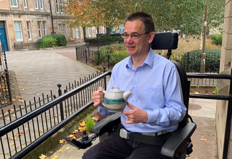 Photo of Paul holding a teapot from his pottery collection.