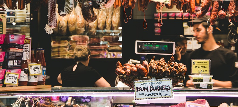 Photo of dried meats shop in a market with sausages and chorizo hanging on top of till and counter.