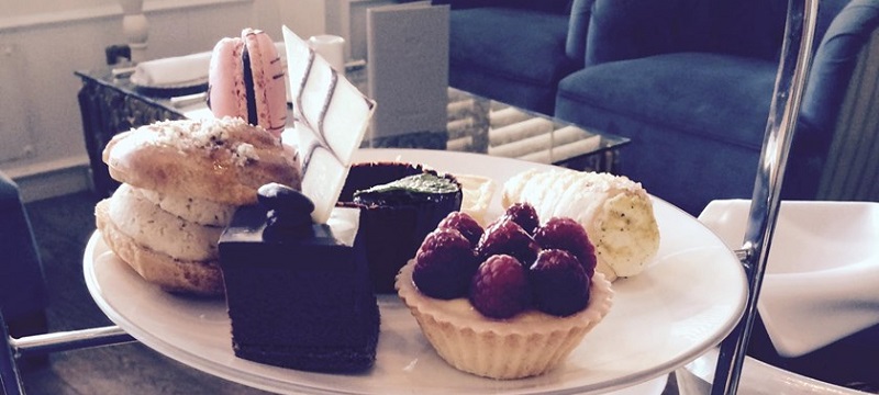 Photo of a tray with six different sweet treats, including a raspberry pie and a macaroons.