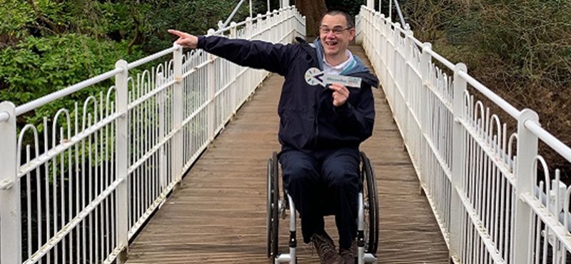 Photo of Paul Ralph holding a Disabled Access Day arrow on a suspension bridge.