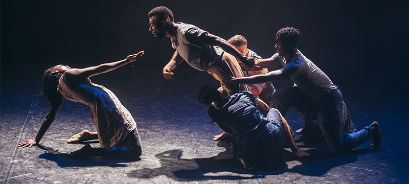 Photo of a Fringe performance - woman on her knees going backwards and a man falling towards her with three men holding him back.