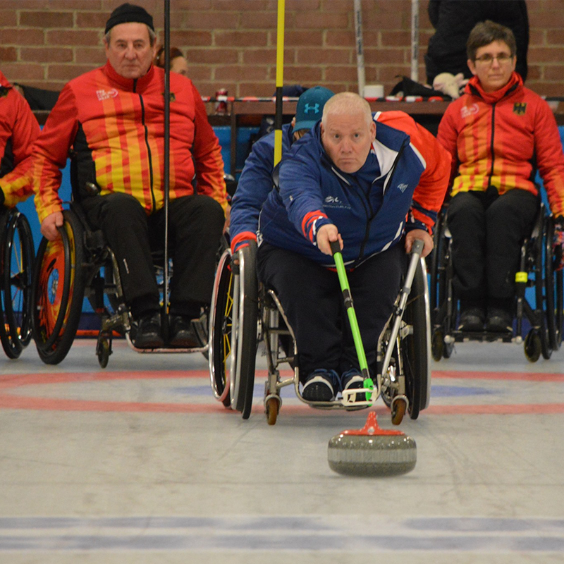 Image of Gary curling with competing team in the background