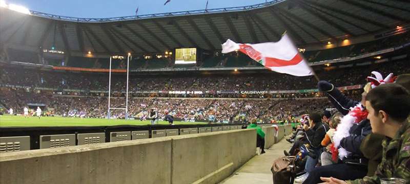 Image of England Rugby flag waving in the wind next to the pitch at Twickenham Stadium.