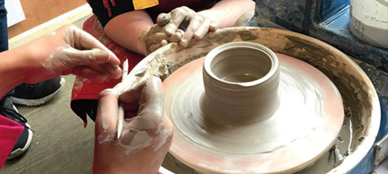 Image of hands working with clay on a pottery wheel.