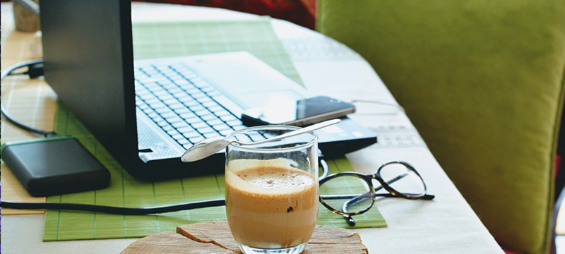 Image of a laptop, coffee, mobile phone and eye glasses on top of a table.