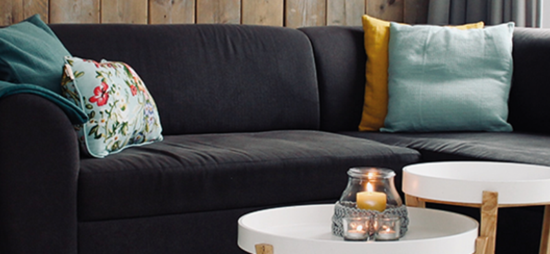 Image of an empty dark sofa with light cushions and a throw over the arm. There is a small circular coffee table infant of the couch.