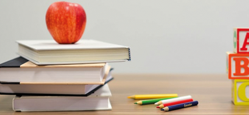 Image of a pile of unnamed books. A red apple is sitting on the books. To the right is lettered alphabet blocks in different colours.