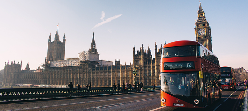 Image of a red bus on a road in front of Big Ben and the Palace of Westminster.