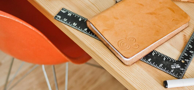 An orange chair next to a desk with rulers, a notebook and pen