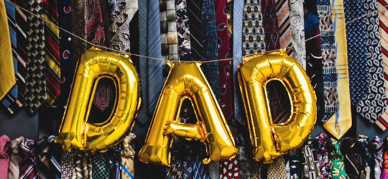 An image of a balloon banner spelling out Dad, in the background there is a wall of ties in various colours.