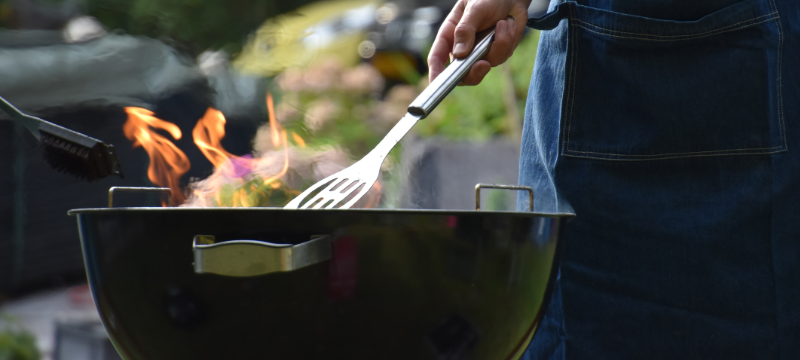 Image of a man holding a spatula while tending to a grill.