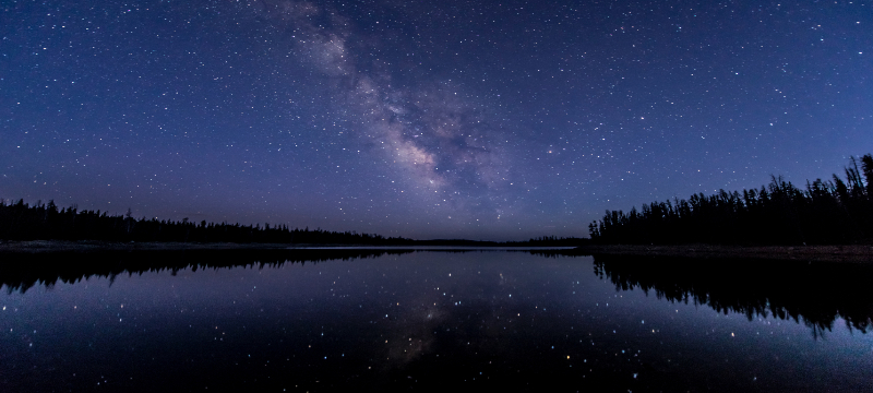 Image of the night sky over a lake that is reflecting the stars.