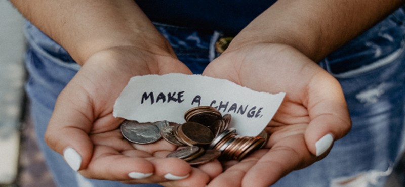 An image of a person holding their hands out with a note that reads 'Make a Change' and some coins. 