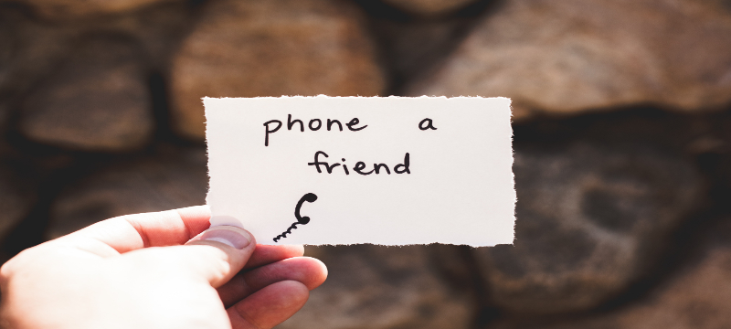 Image of a person holding out a note that reads 'Phone a friend'