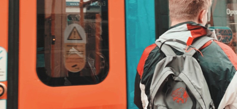 Someone waiting to board the train with their back to the camera wearing a backpack