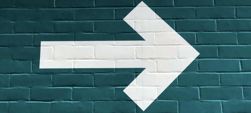 A teal brick wall with a white arrow painted on pointing right.