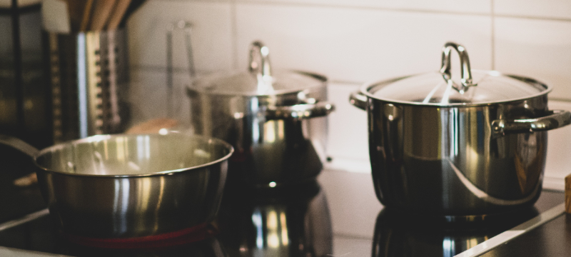 A selection of 3 stainless steel pots and pans on an induction hob.