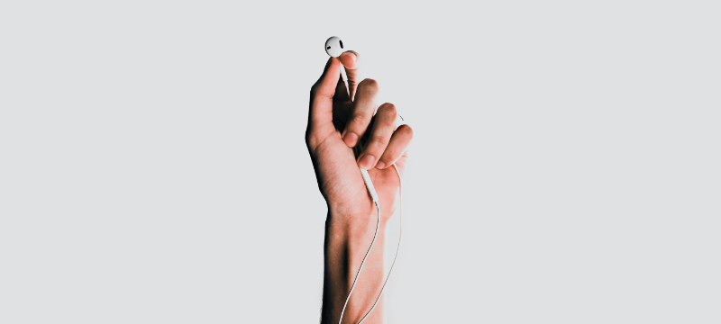 A light background with a hand in the centre of the image with earphones held between their fingers.