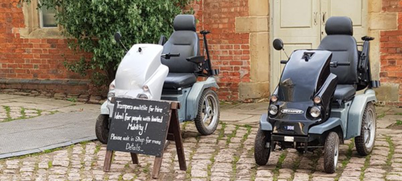 Two trampers pictured next to each other on cobbled ground. There is a black sign with white writing on it in front of one of the trampers.