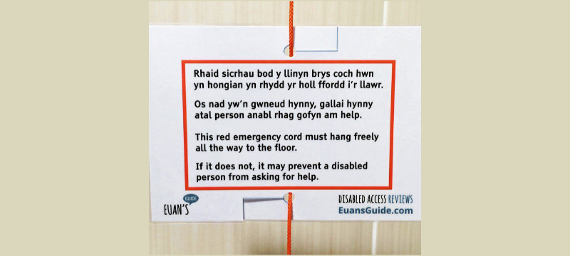 A Red Cord Card with text shown in Welsh at the top and an English translation shown below. The text in English reads " This red emergency cord must hang freely all the way to the floor. If it does not, it may prevent a disabled person from asking for help."
