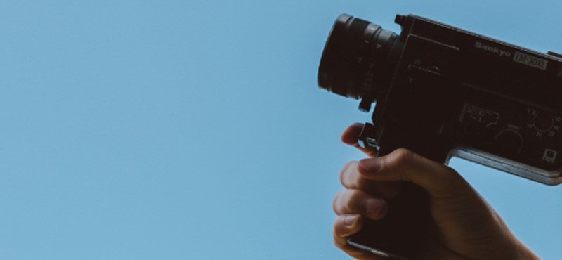 A film camera held up against a blue sky