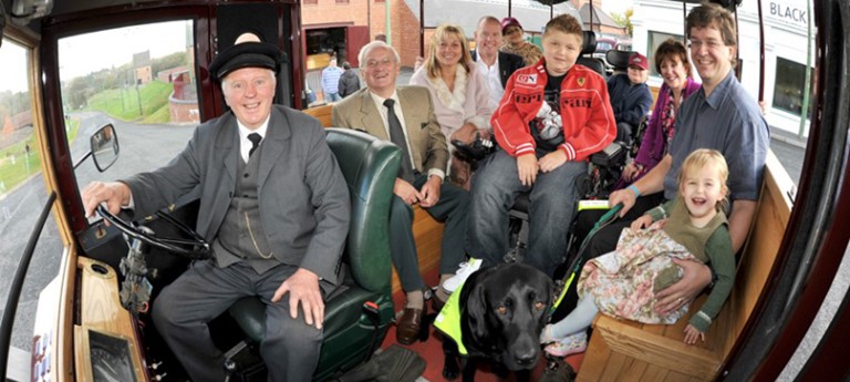 An old fashioned bus filled with people, including wheelchair and powerchair users and an assistance dog.