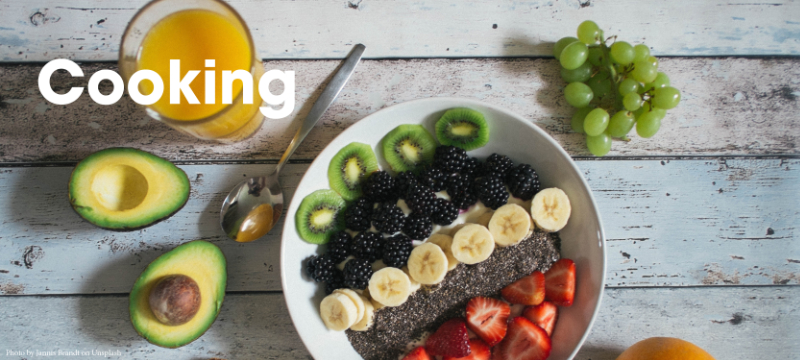 A picture of fruit in and around a bowl. The background is a painted wood and the word "Cooking" is written on top of the image.