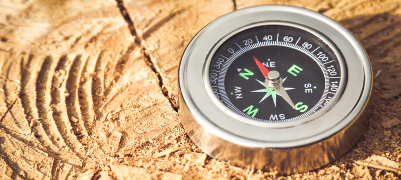 A close up picture of a compass with a silver casing on a wooden surface.