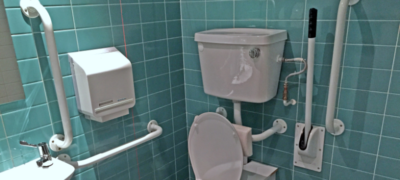 An accessible toilet with green tiles on the wall.