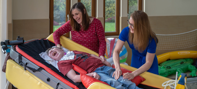 James is pictured lying down. Christine and Helen are both standing behind him with their hands on him.