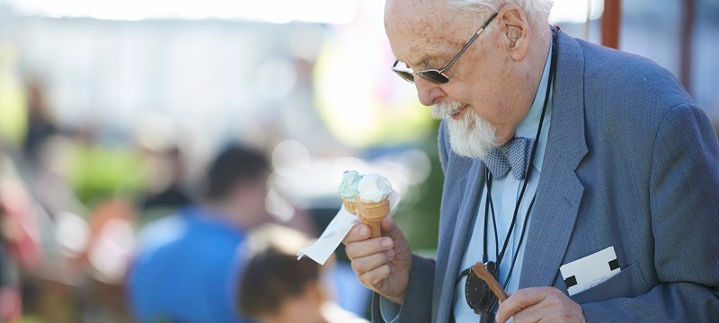Elderly man with glasses and hearing aid holds an ice cream.
