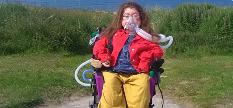 Photo of Karis sitting in her wheelchair infront of grass