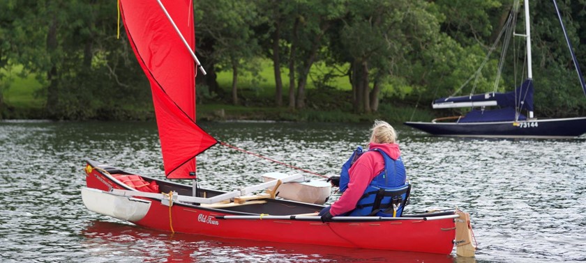 Person sailing boat in a body of water with trees in the background.