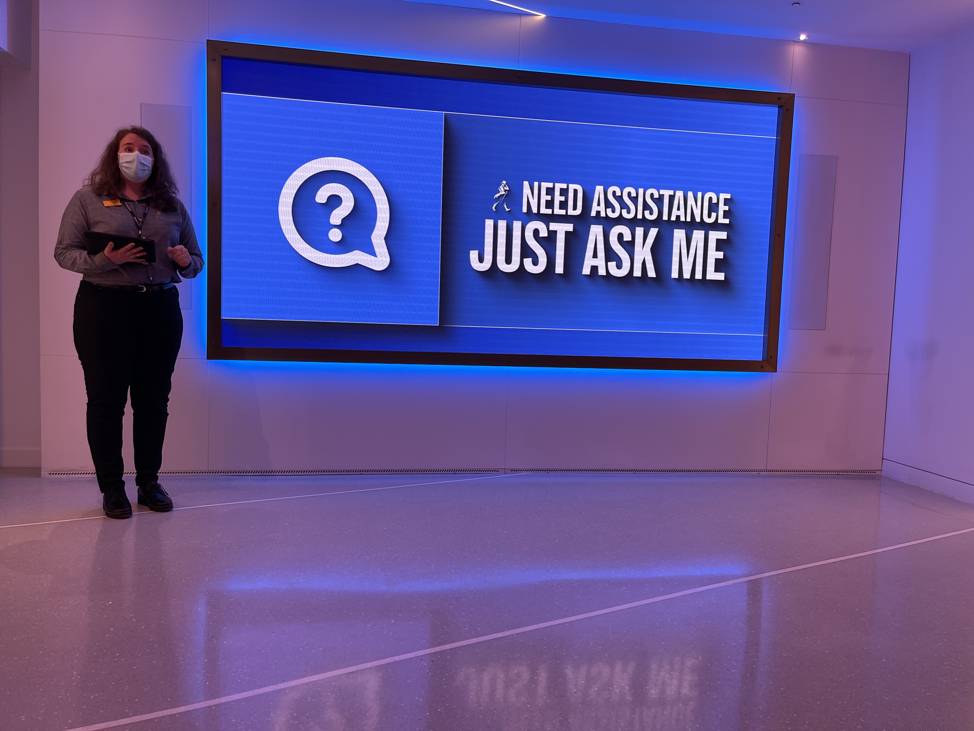 A Johnnie Walker Princes Street staff member standing next to a screen which says "Need Assistance, Just Ask Me".