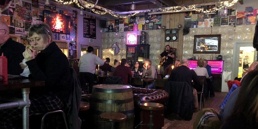 A person playing guitar to a crowd while some eat at Saint Luke's