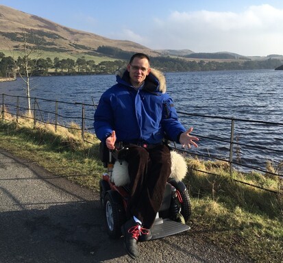 Paul Ralph on the path next to a reservoir at the Pentlands with a hill in the background.