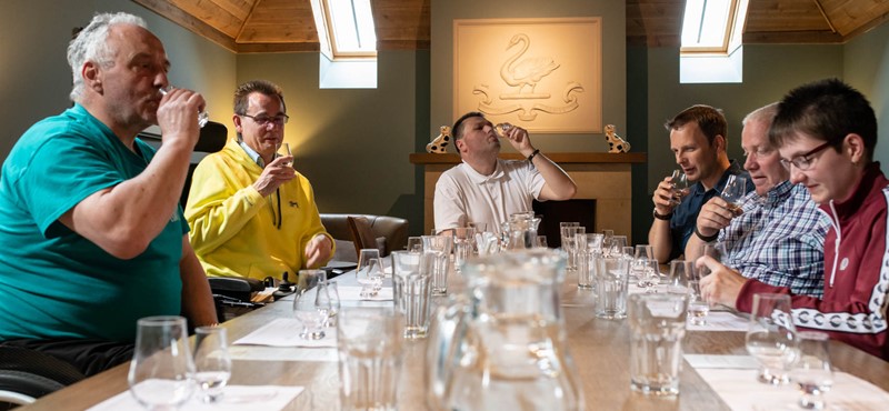 Six people around a table doing whisky tasting.